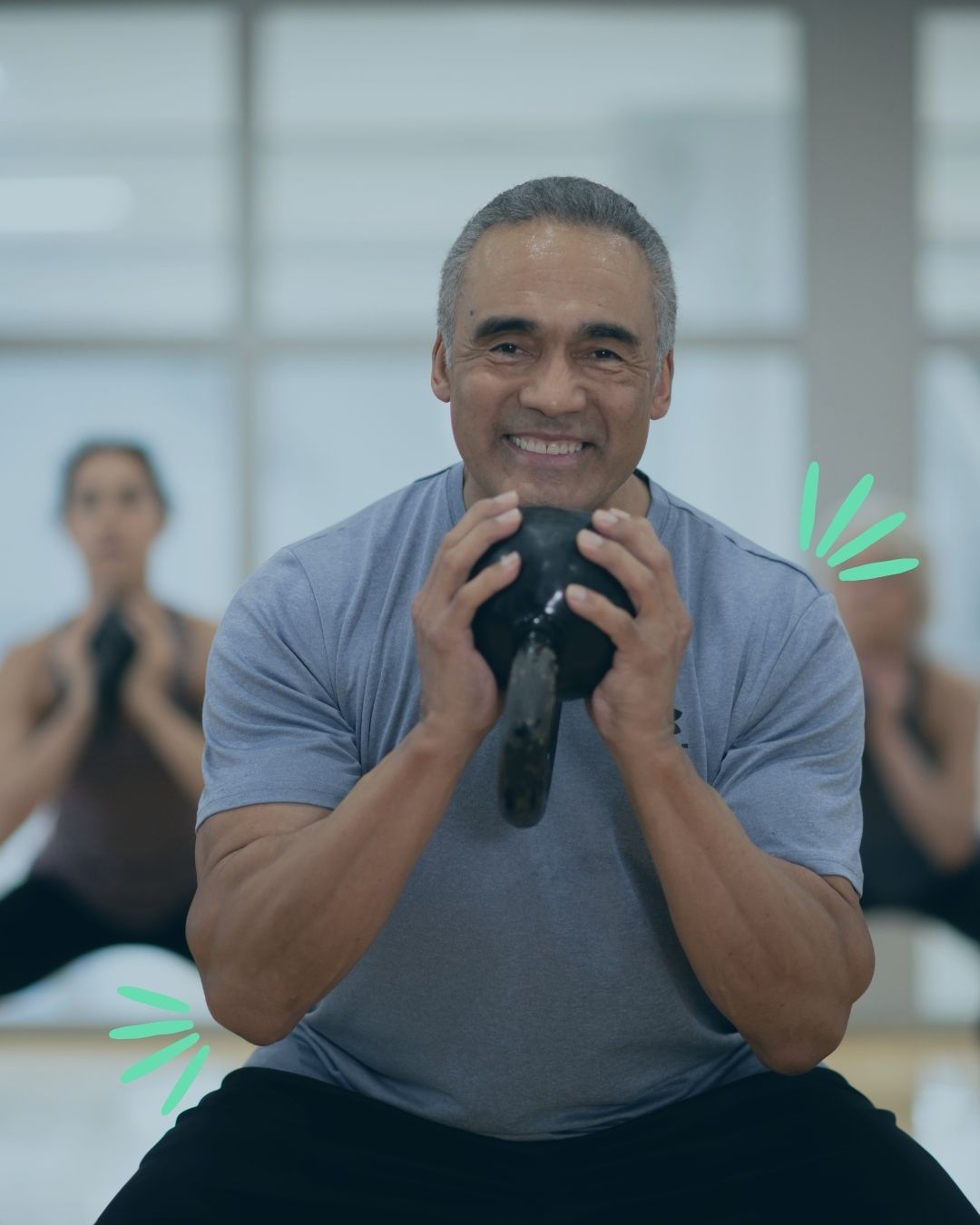 older man working out in group fitness class lifting a kettle bell and smiling, he feels supported by cws services