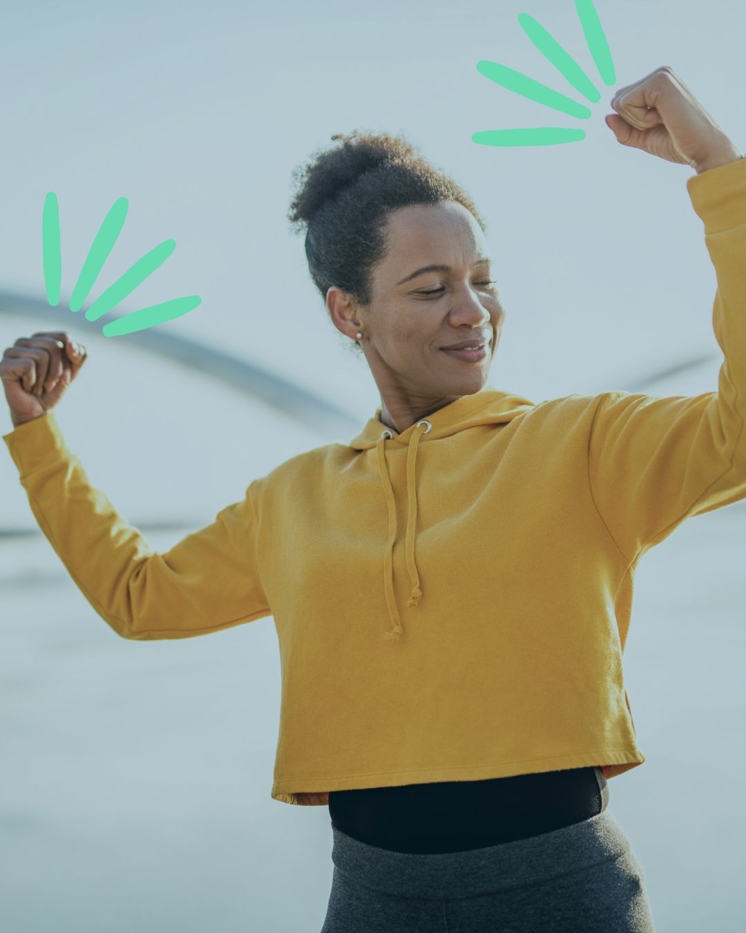 Middle aged woman in yellow hoodie strikes pose flexing arms, she looks happy and empowered reflecting what CWS is about- personal strength and resilance